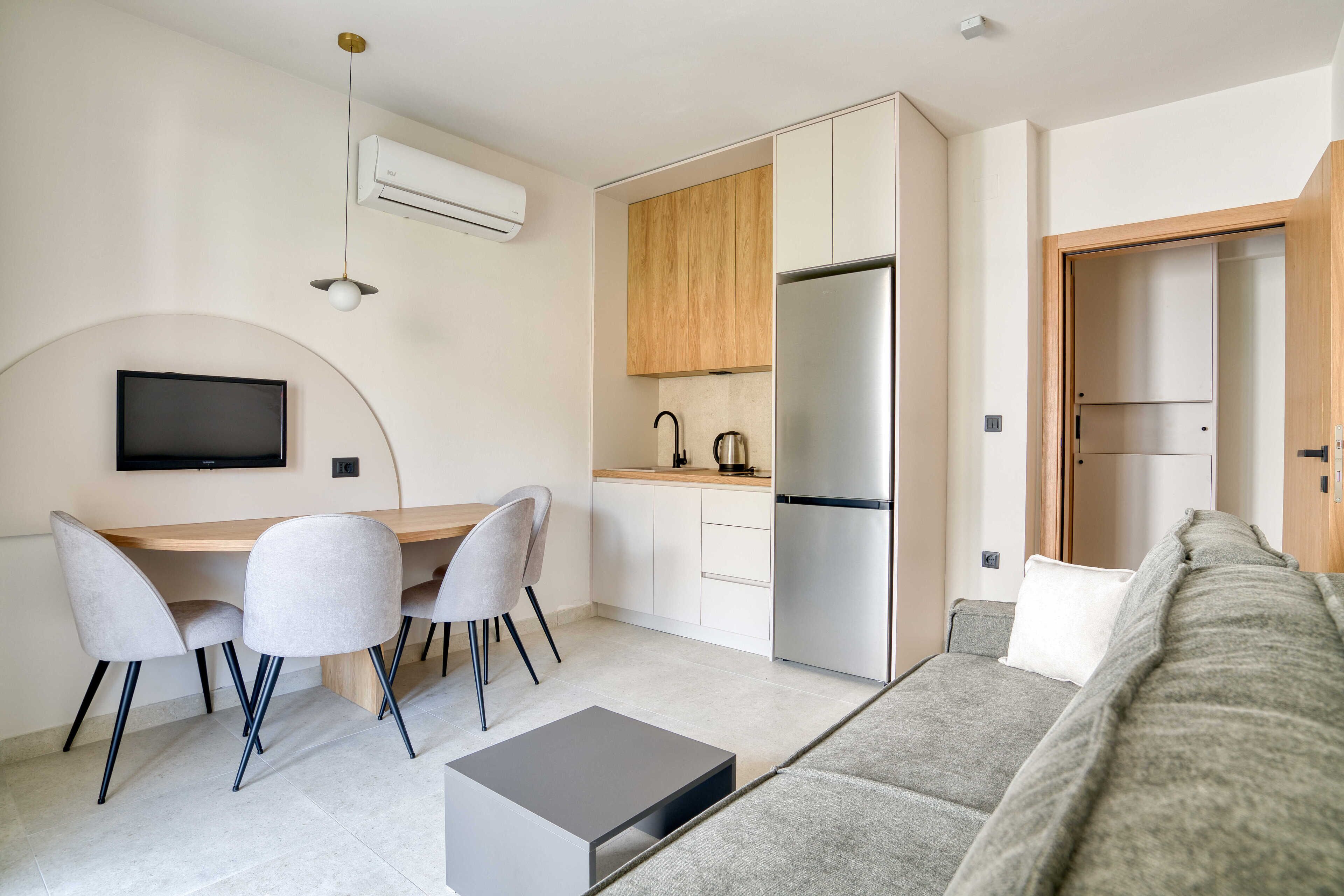 A compact living space with a kitchenette, a dining area, a sofa, and a flat-screen TV.