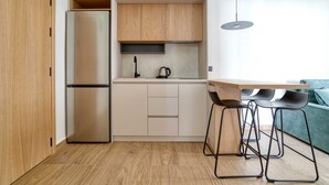 A compact kitchen with a built-in refrigerator, wooden cabinets, a coffee maker, and a bar stool. - Mont Residence (Budva)