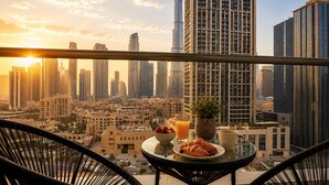 A balcony with a table set for breakfast, overlooking a cityscape with high-rise buildings and a clear sky. - Luxury Downtown Skyline Suite Burj Khalifa View (Dubai)