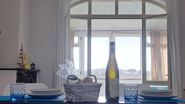 A dining area with a table set for two, a bottle of wine, and a view through a window. - A standalone apartment just a few minutes from downtown Ischia. (Ischia)
