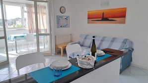 A dining area with a table set for two, a sofa, a clock, and a painting of a lighthouse. - A standalone apartment just a few minutes from downtown Ischia. (Ischia)