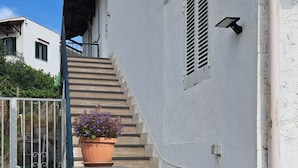 A white building with a staircase leading to a door, a potted plant, and a metal gate. - A standalone apartment just a few minutes from downtown Ischia. (Ischia)