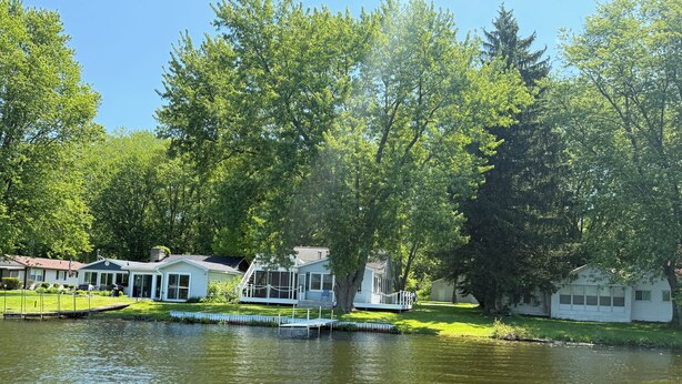 A lakeside cabin with a dock, surrounded by lush greenery and trees.