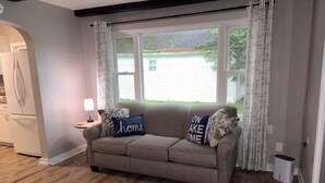 A living room with a grey sofa, a lamp, and a window with curtains.