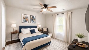 Un dormitorio con cama, mesitas de noche, ventilador de techo, obras de arte, una ventana con cortinas y una planta.