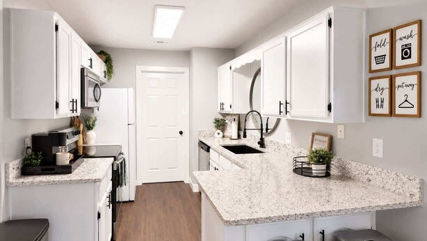 Una cocina moderna con gabinetes blancos, encimera de granito, un lavamanos y taburetes de bar.