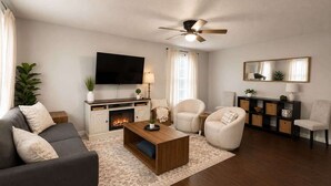 Una sala de estar con chimenea, televisor, ventilador de techo y sofá.