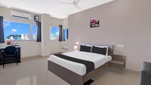 A hotel room with a bed, desk, chair, and a view of buildings. - Deluxe Cloud Stay (Guwahati)