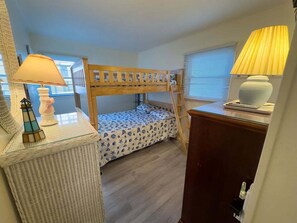 Ein Kinderstockbett mit einem gemusterten Bettbezug, ein kleiner Tisch mit Lampe sowie eine Kommode mit Lampe.