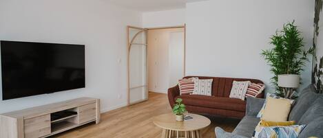 Un salon moderne avec un téléviseur à écran plat, un meuble de rangement en bois, une table basse ronde, un canapé marron, un canapé gris et une grande plante.