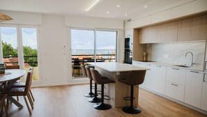 Una cuina moderna amb una illa gran, tamboretes i vista al mar.