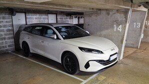 Un cotxe blanc estacionat en una plaça numerada dins un edifici amb parets de formigó i portes amb números.
