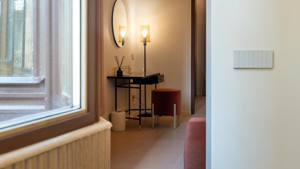 A hallway with a radiator, a mirror, a desk with a lamp, a red stool, and a white switchboard. - Luxury designer suites just a short walk from the Spanish Steps (Roma)