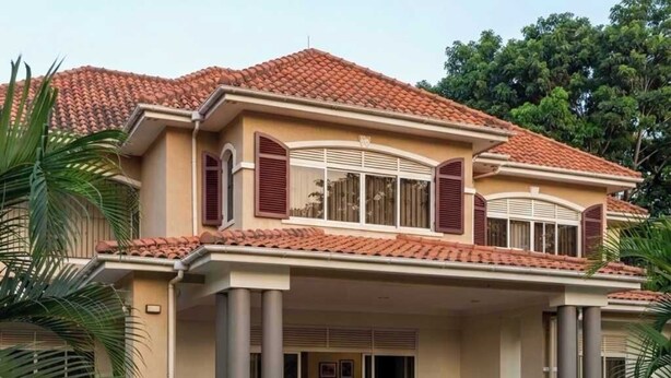 A two-story house with a tiled roof, a covered front porch, and a landscaped front yard. - TyCounty Boulevard Apartments (Bulanga)