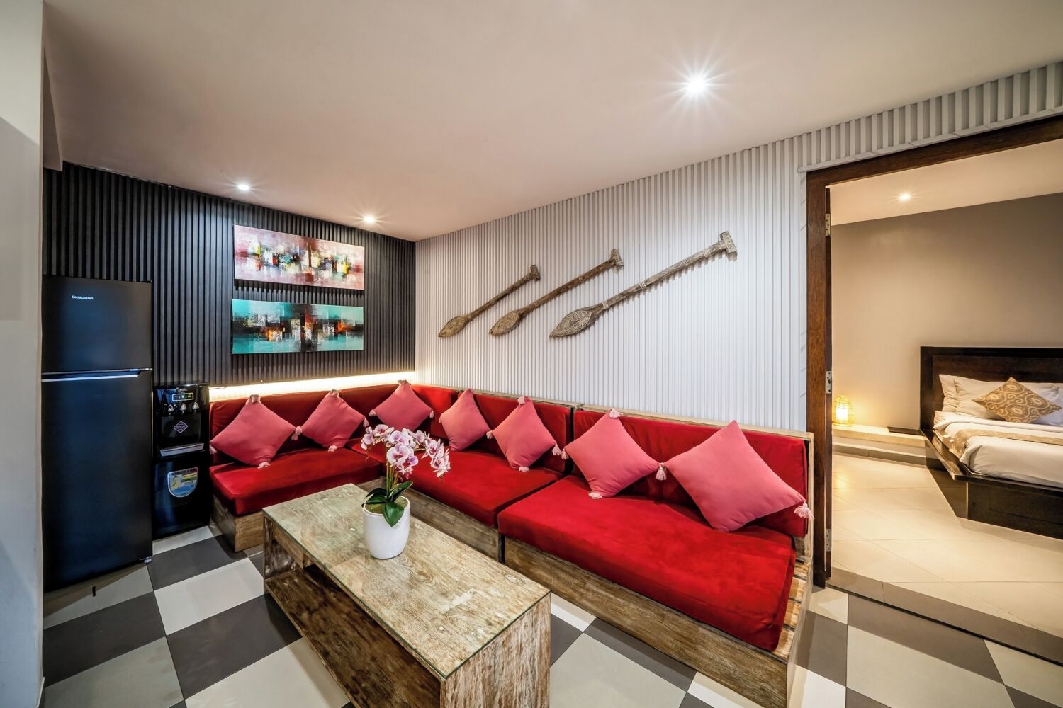 Un salon moderne avec un canapé rouge, une table basse en bois, un réfrigérateur et un téléviseur fixé au mur.