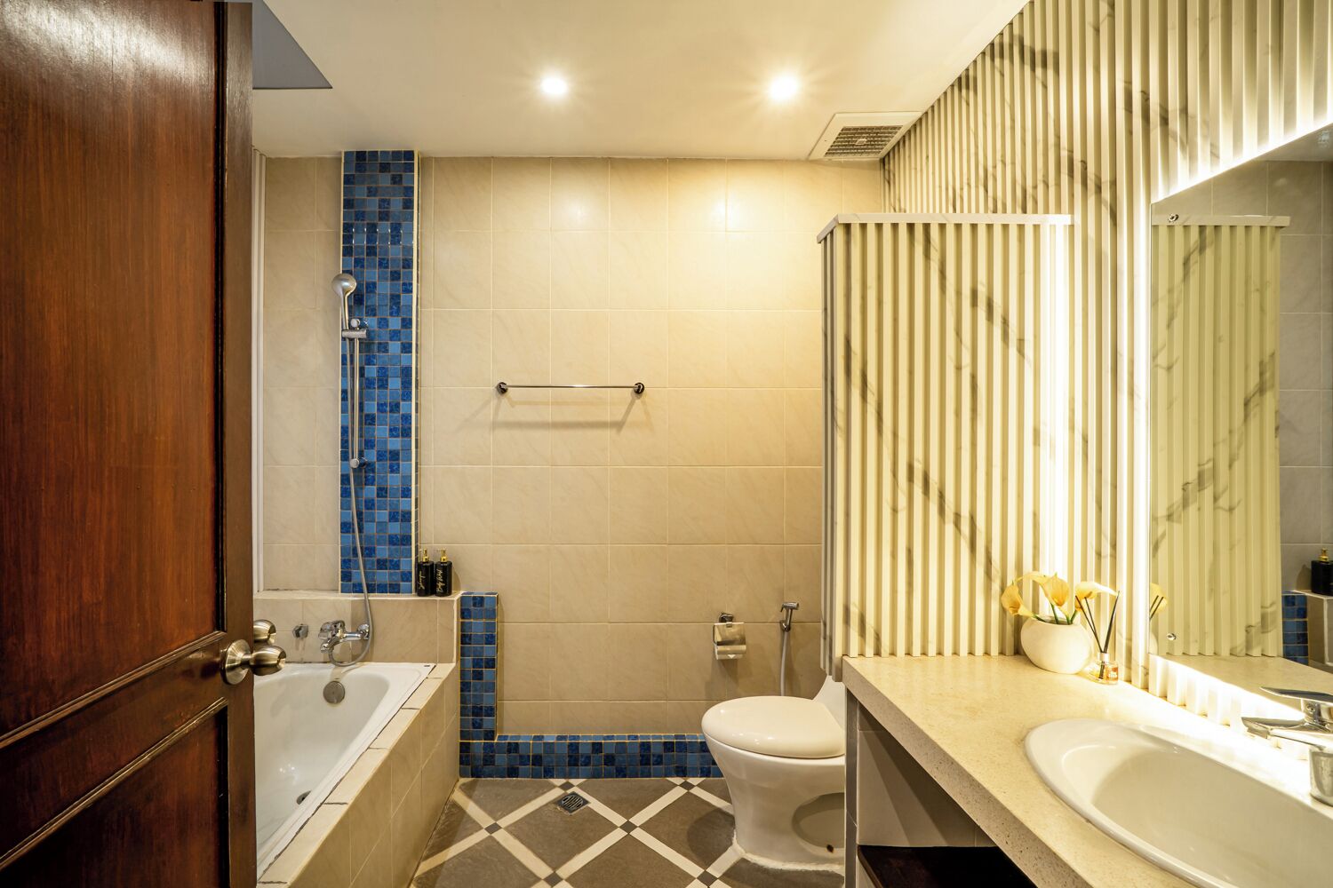 A bathroom with a bathtub, toilet, and sink, featuring a blue-tiled shower area and a striped wall design.