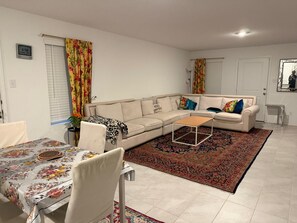 Un salon comprenant un canapé, une table basse, une table à manger avec des chaises et un tapis à motifs.