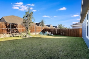 Un jardin avec une clôture en bois, une pelouse et un espace patio aménagé avec des chaises.