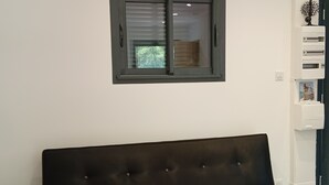 A modern room with a dark sofa, a window with blinds, a white wall, and a small shelf with items. - A little slice of paradise, nestled in the woods (Ste Baume, Canal de Provence, ... (Rougiers)