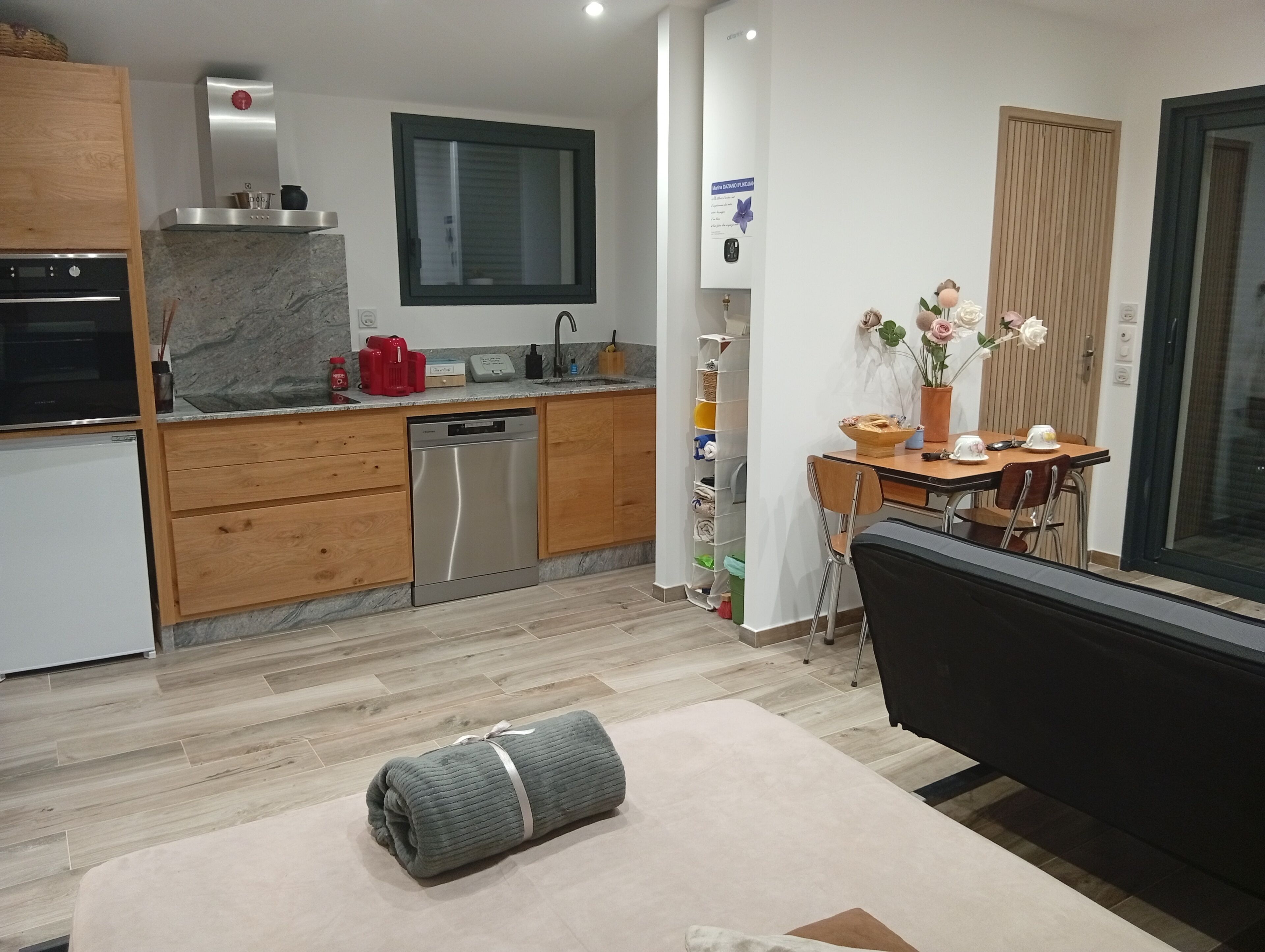 Ett modernt kök med träskåp, en inbyggd diskmaskin och en matplats med bord och stolar.