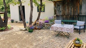 A rustic outdoor area with a small white building, a wooden table with a patterned tablecloth, and a chair. - A little slice of paradise, nestled in the woods (Ste Baume, Canal de Provence, ... (Rougiers)