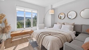 Un dormitorio con una ventana grande, una cama, una mesita de noche, una silla y un sofá.