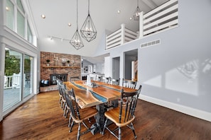 A spacious dining area with a long wooden table and chairs, a brick wall, and large windows. - Lake Front Home, Huge fun dock & Hot Tub! (Sunrise Beach)