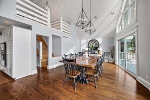 A spacious dining area with a wooden table and chairs, a staircase leading to an upper level, and a large window providing a view of the outdoors. - Lake Front Home, Huge fun dock & Hot Tub! (Sunrise Beach)