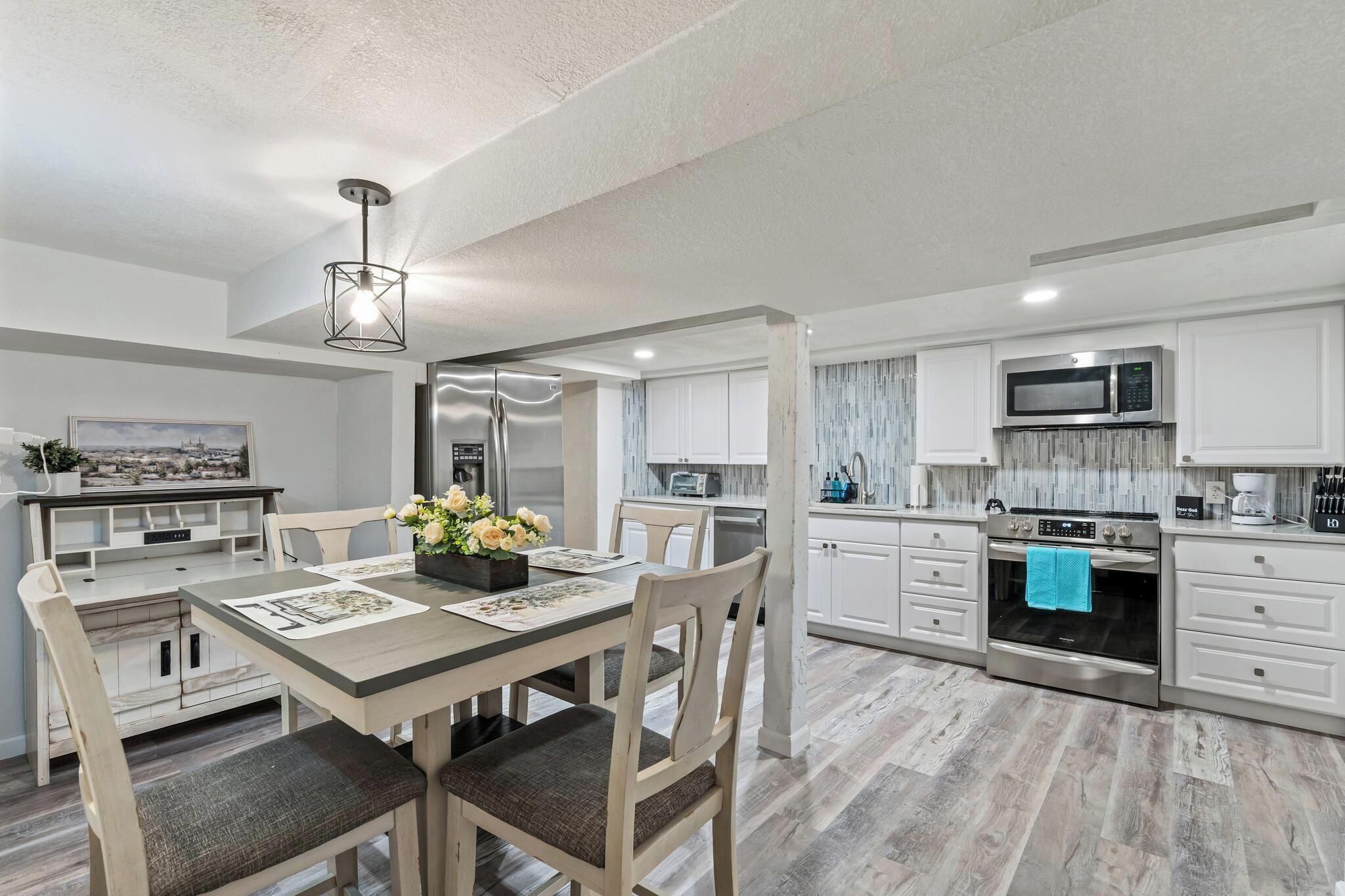 A modern kitchen with stainless steel appliances, a dining area with a wooden table and chairs, and a view of the cityscape through the window.