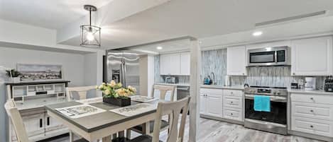 A modern kitchen with stainless steel appliances, a dining area with a wooden table and chairs, and a view of the cityscape through the window.