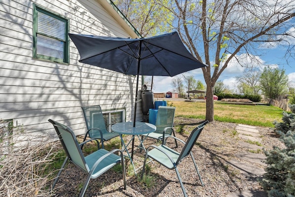 An outdoor patio with a table and chairs, a large umbrella, and a house in the background.