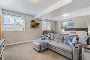 A bedroom with a large bed, a sofa, and a small table. There are windows with blinds, a ceiling light, and a wall-mounted plant. - Light-Filled Lower Level with Private Entry on 2 Acres, Close to Shops (Arvada)