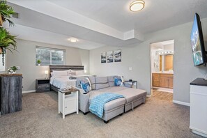 Ein modernes Schlafzimmer mit einem Bett, einem grauen Sofa, einem Nachttisch und einem Beistelltisch.