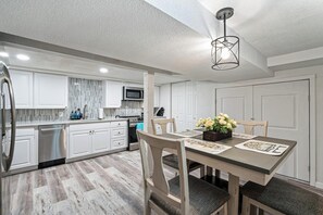 A modern kitchen with white cabinetry, a dining table with floral placemats, and a hanging light fixture.