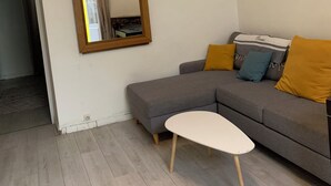 En stue med en grå sofa, et lille hvidt bord og et spejl på væggen.
