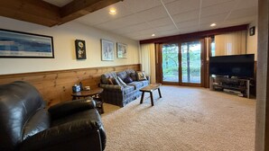 A living room with a leather sofa, a wooden coffee table, a television, and a large window with a view of trees. - Wine'd Down on Lake Waukewan- New Lisiting- Photos Updated (Meredith)