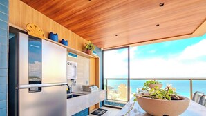 A modern kitchen with a stainless steel refrigerator, a coffee machine, and a view of the ocean through large windows. - Relax in an ocean view apartment in Barra (Salvador)