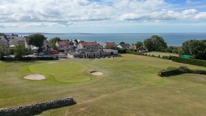 A golf course with a clubhouse, houses in the background, and a view of the sea.