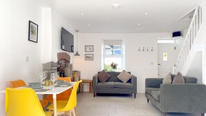 A modern living room with a grey sofa, yellow chairs, a dining table set, and a TV mounted on the wall.