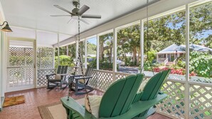 A covered porch with a swing chair, a ceiling fan, and a view of the surrounding greenery and buildings.
