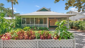 A house with a covered porch, a fenced garden, and a clear blue sky.