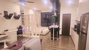 A modern living room with a sofa, a desk, a chair, a dining table, and a kitchen area with a refrigerator. - Landmark Residence I Kajang I City View (Kajang)