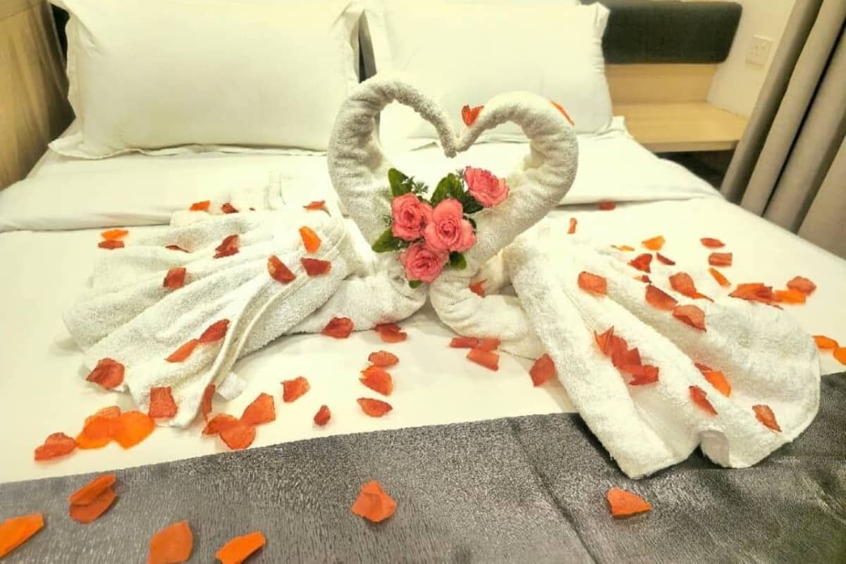 Uma cama com arranjo de toalha em formato de coração e pétalas de rosa.