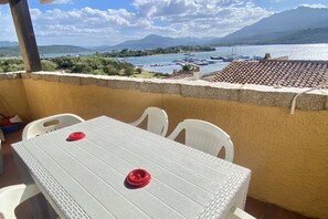 A balcony with a table and chairs, overlooking a marina with boats and a mountainous landscape. - P. Rotondo 1 I234 SEA VIEW Studio (Porto Rotondo)