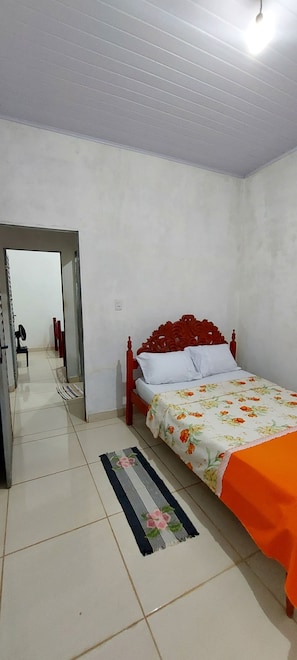 Ein Schlafzimmer mit Bett, Spiegel, Tür und einem zur angrenzenden Kammer führenden Flur.