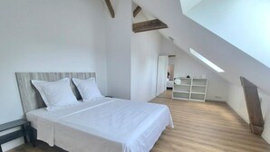 Une chambre à coucher avec un lit, un plancher en bois, des murs blancs et un puits de lumière.