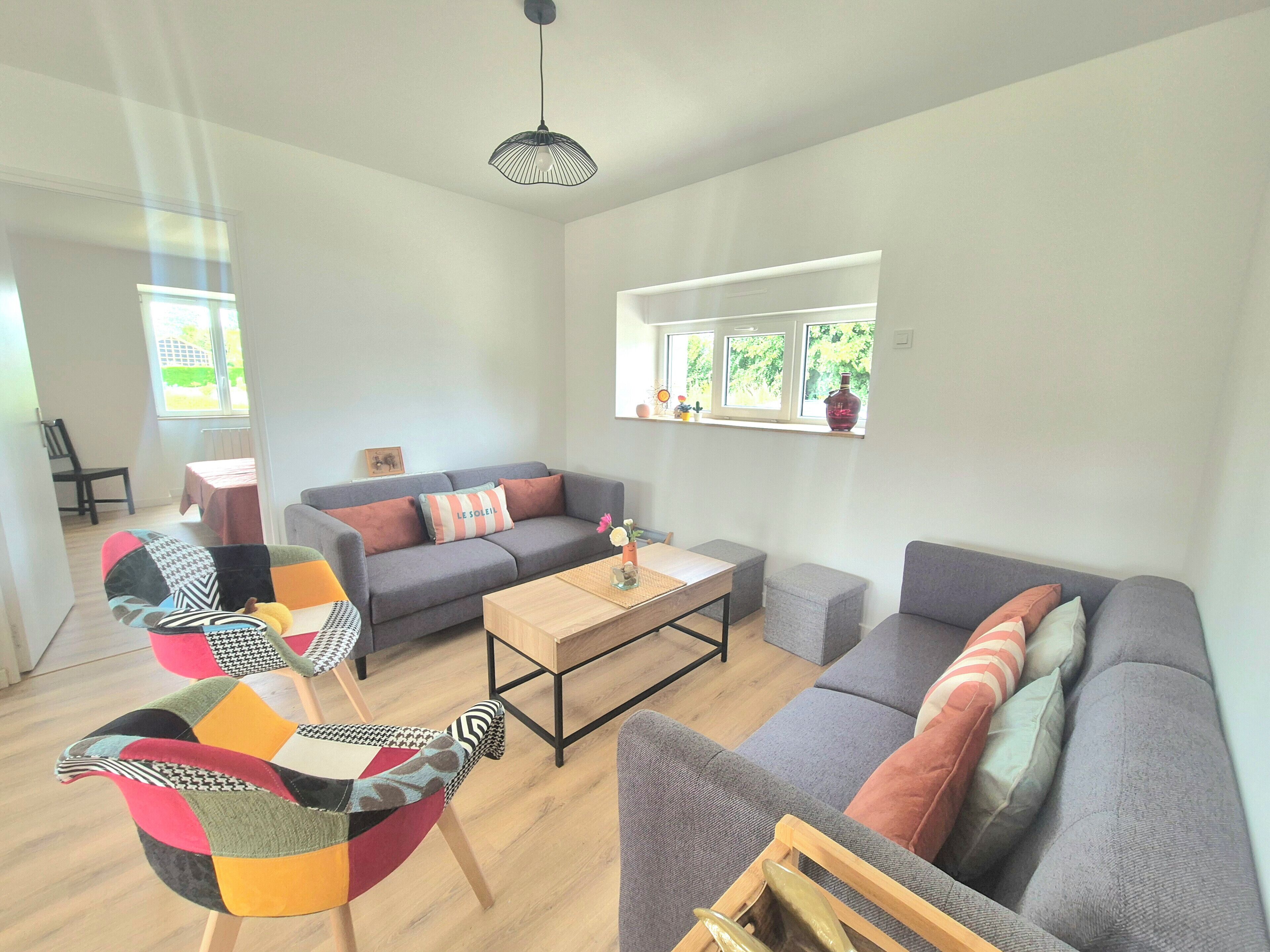 Una sala moderna con un sofá gris, un sillón colorido y una mesa de centro de madera.