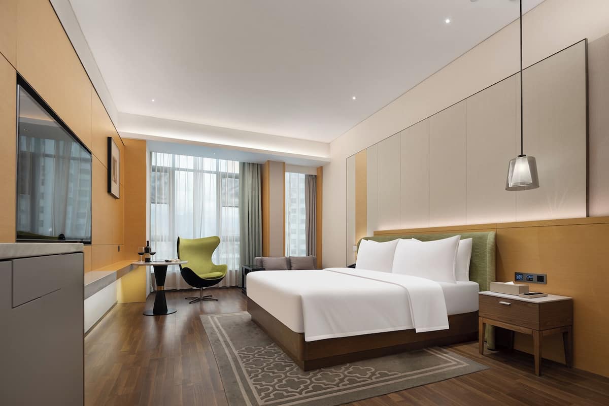 Ein modernes Hotelzimmer mit einem großen Bett, einem Schreibtisch, einem Stuhl und einem großen Fenster.