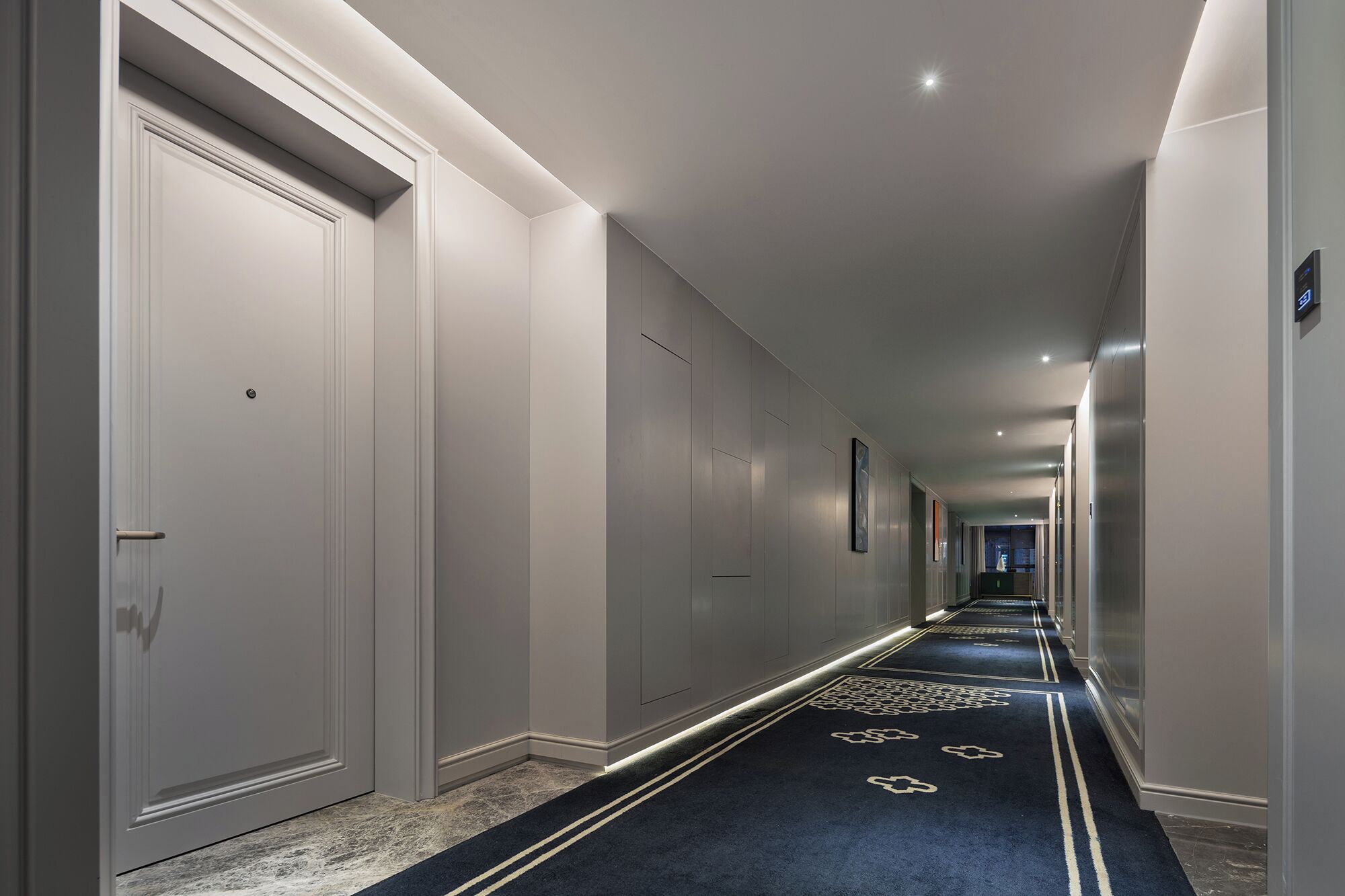 A long, narrow hallway with a carpeted floor, white walls, and doors on one side.