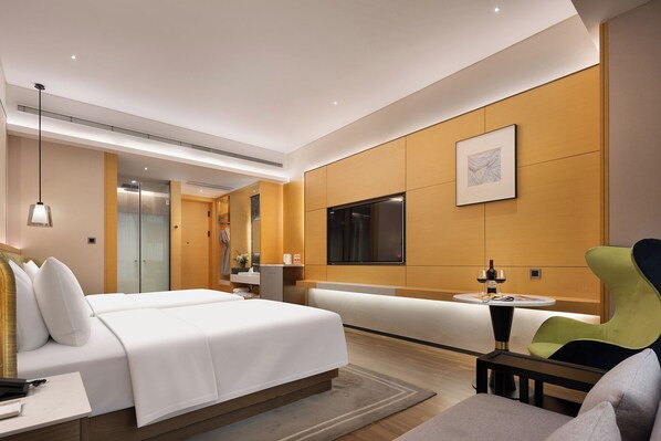 A modern hotel room with a bed, a seating area, a television, and a bathroom.